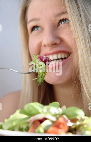 Young blonde woman eating salad, smiling Banque D'Images