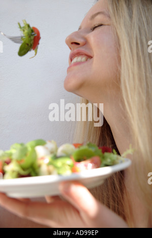 Young blonde woman eating salad, smiling Banque D'Images