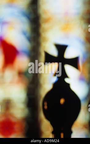 Gros plan d'une croix en laiton surmontant un orb et silhouetté contre l'église de vitraux lointain windows Banque D'Images