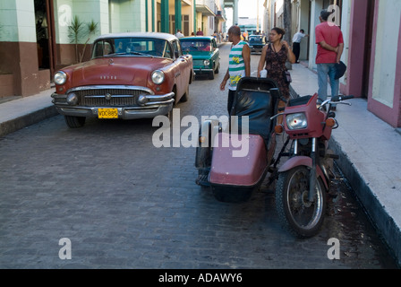 Les voitures en stationnement et les piétons dans une rue pavée, à Santa Clara, Villa Clara, Cuba. Banque D'Images