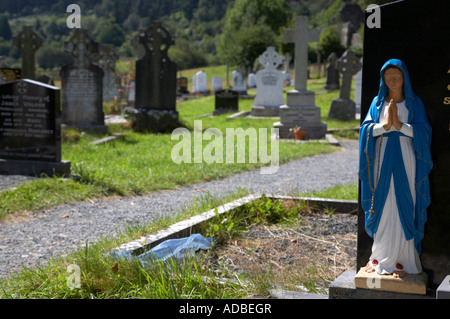 Le bleu et blanc statue de Notre Dame la Vierge Marie prier assis sur le dessus d'une fosse dans le cimetière du monastère de Glendalough Banque D'Images