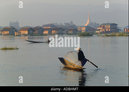 Pêcheur ethnie Intha bateau à rames avec une jambe, village et pagode à la distance, au Lac Inle, Myanmar Banque D'Images