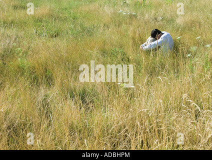 Homme assis dans le champ, serrant les genoux, la tête en bas Banque D'Images