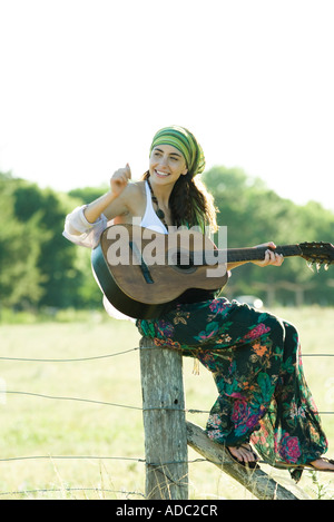 Jeune hippie woman sitting on fence post, à jouer de la guitare Banque D'Images