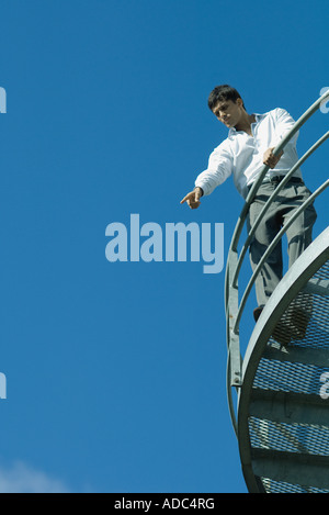 Businessman standing on metal balcon, orientée vers le bas, low angle view, ciel bleu en arrière-plan Banque D'Images