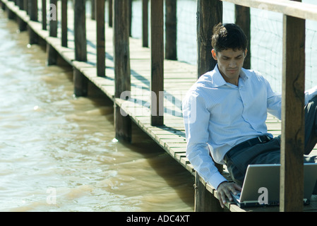 Businessman on wooden passerelle au-dessus de lac, using laptop Banque D'Images