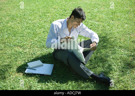 Businessman sitting on grass, reading newspaper Banque D'Images