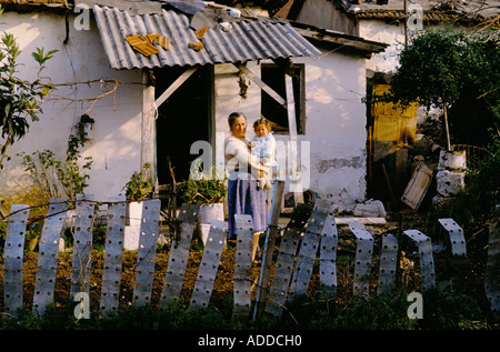 WOMAN HOLDING BABY DANS LE JARDIN DE DEVANT DE LA PETITE MAISON délabrée, Saranda, 1993, Banque D'Images