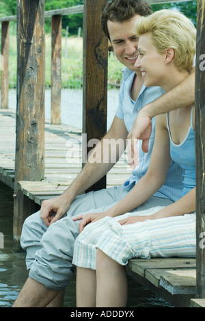 Couple assis sur la passerelle en bois, balançant les pieds dans l'eau Banque D'Images