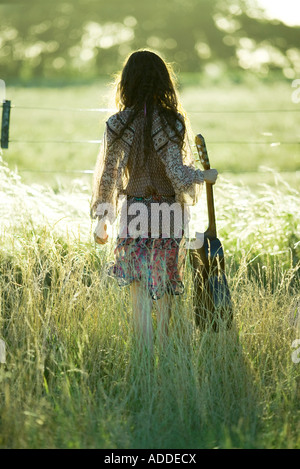 Young woman holding hippie guitare, standing in field, vue arrière Banque D'Images