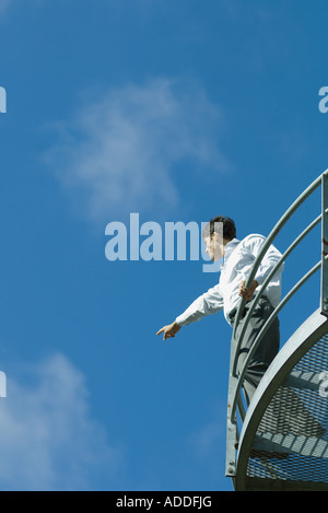 Businessman standing on metal balcon, se dirigeant à distance, low angle view, ciel bleu en arrière-plan Banque D'Images