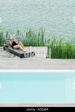 Jeune femme allongée sur une chaise longue, d'une lecture Banque D'Images