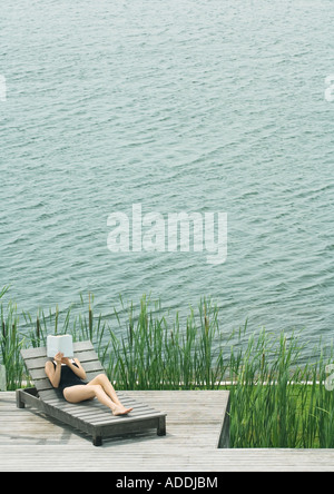 Jeune femme allongée sur une chaise longue, d'une lecture Banque D'Images