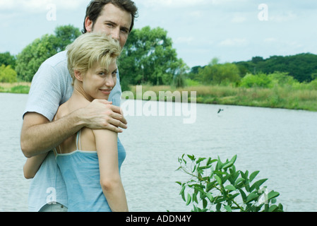 Couple standing par le lac, à la recherche sur les épaules à l'appareil photo Banque D'Images