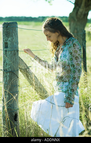 Jeune femme debout à côté d'une clôture rurale, regardant vers le bas Banque D'Images