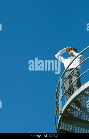 Businessman standing on metal balcon, regardant ailleurs, low angle view, ciel bleu en arrière-plan Banque D'Images