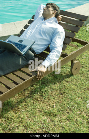 Woman reclining on lounge chair, ordinateur portable sur les genoux, les yeux fermés Banque D'Images