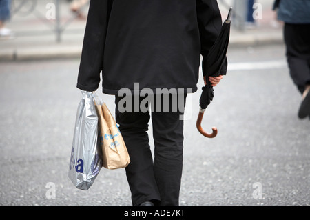 Seul businessman crossing road transportant des sacs de magasinage et parapluie Banque D'Images