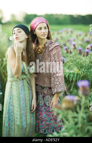 Les jeunes femmes hippie standing in field, l'un souffle les graines de pissenlit Banque D'Images
