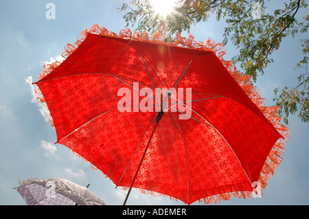 Frog eye view de frilly fiery red parasol contre ciel bleu avec du soleil Banque D'Images