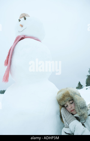Teen girl resting head contre snowman Banque D'Images