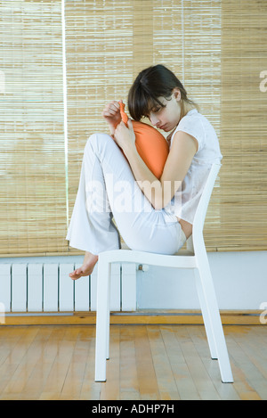 Jeune femme assise sur un fauteuil avec Coussin genoux, holding Banque D'Images