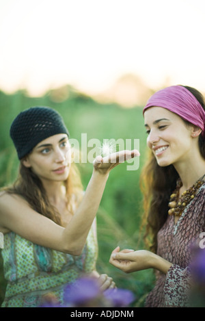 Deux jeunes femmes à l'extérieur, un holding dandelion seed head sur la paume de la main Banque D'Images