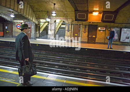 Man wearing hat et costume attend pour former sur le métro de Londres Banque D'Images