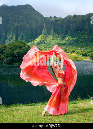Danseuse du Ventre avec voile rouge, bras tendus au décor tropical Banque D'Images