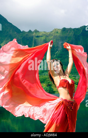 Danseuse du Ventre avec voile rouge, bras tendus au décor tropical Banque D'Images