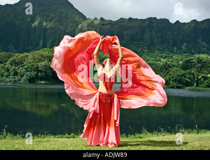 Danseuse du Ventre avec voile rouge, bras tendus au décor tropical Banque D'Images