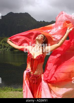 Danseuse du Ventre avec voile rouge, bras tendus au décor tropical Banque D'Images