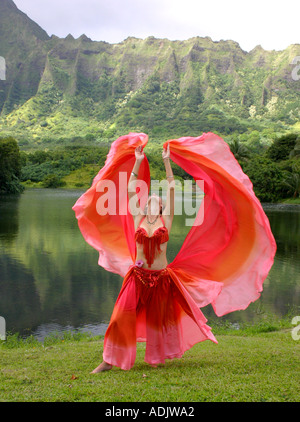 Danseuse du Ventre avec voile rouge, bras tendus au décor tropical Banque D'Images