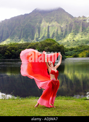 Danseuse du Ventre avec voile rouge, bras tendus au décor tropical Banque D'Images