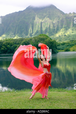 Danseuse du Ventre avec voile rouge, bras tendus au décor tropical Banque D'Images