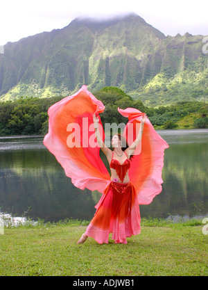 Danseuse du Ventre avec voile rouge, bras tendus au décor tropical Banque D'Images