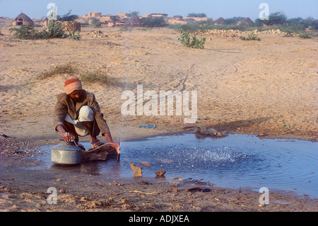 Pénurie d'eau, homme qui collecte de l'eau d'un tuyau qui fuit en utilisant un petit tuyau pour remplir le pot, Rajasthan, INDE, Asie Banque D'Images