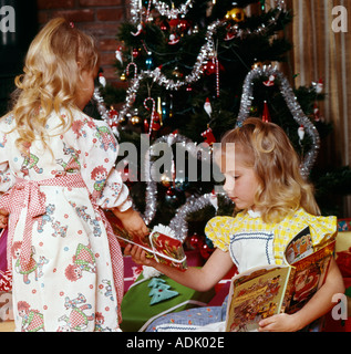 Deux jeunes sœurs à la présente au sous un arbre de Noël décoré gaiement Banque D'Images