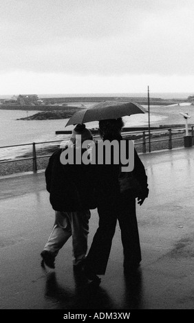 Couple en train de marcher sous la pluie sur le front de mer Banque D'Images