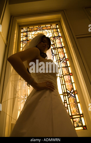 Habillé traditionnellement bride holding bouquet floral en face de l'église à l'intérieur fenêtre stainglass Banque D'Images