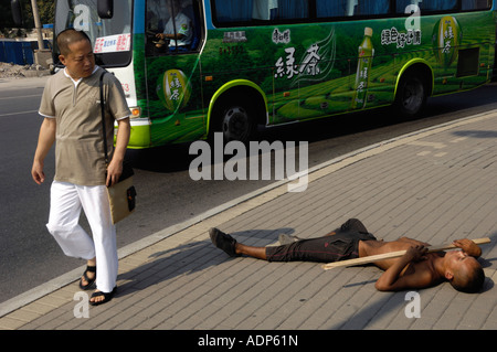 Un homme passe devant un jeune mendiant couché sur le bord de la route à Beijing, en Chine, 15 août 2007 Banque D'Images