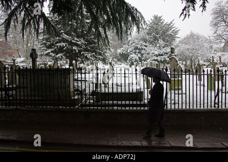 Homme avec parapluie marche dernières couvertes de neige cimetière Hampstead London United Kingdom Banque D'Images