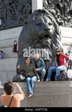 Des touristes posent pour des photos sur lion statue à la base de la Colonne Nelson de Trafalgar Square London UK Banque D'Images