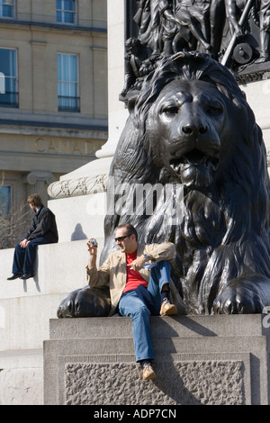 Siège de tourisme de prendre des photographies sur des statues de lion à la base de la Colonne Nelson de Trafalgar Square London UK Banque D'Images