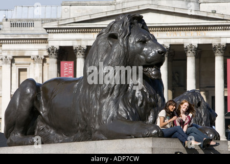 Les touristes s'asseoir sur des statues de lion en face de la National Gallery à Trafalgar Square London United Kingdom Banque D'Images