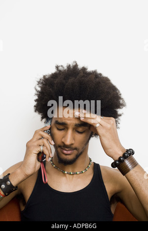 Homme à l'afro et bracelets talking on cell phone with hand on head Banque D'Images