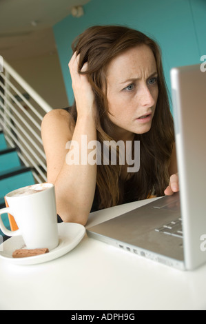 Jeune femme aux cheveux rouges à la recherche dans l'incrédulité à l'ordinateur portable dans un bar café consulter la messagerie web surf Banque D'Images