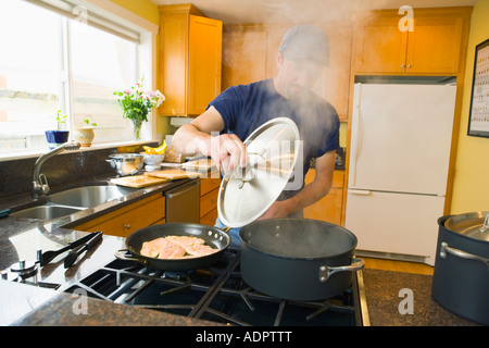 L'augmentation de vapeur à partir de la casserole sur la cuisinière pendant que les cuisiniers de l'homme dans sa cuisine Banque D'Images