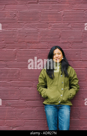 Portrait of smiling young woman leaning against wall marron Banque D'Images