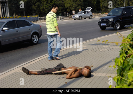 Un homme passe devant un jeune mendiant couché sur le bord de la route à Beijing, en Chine, 15 août 2007 Banque D'Images